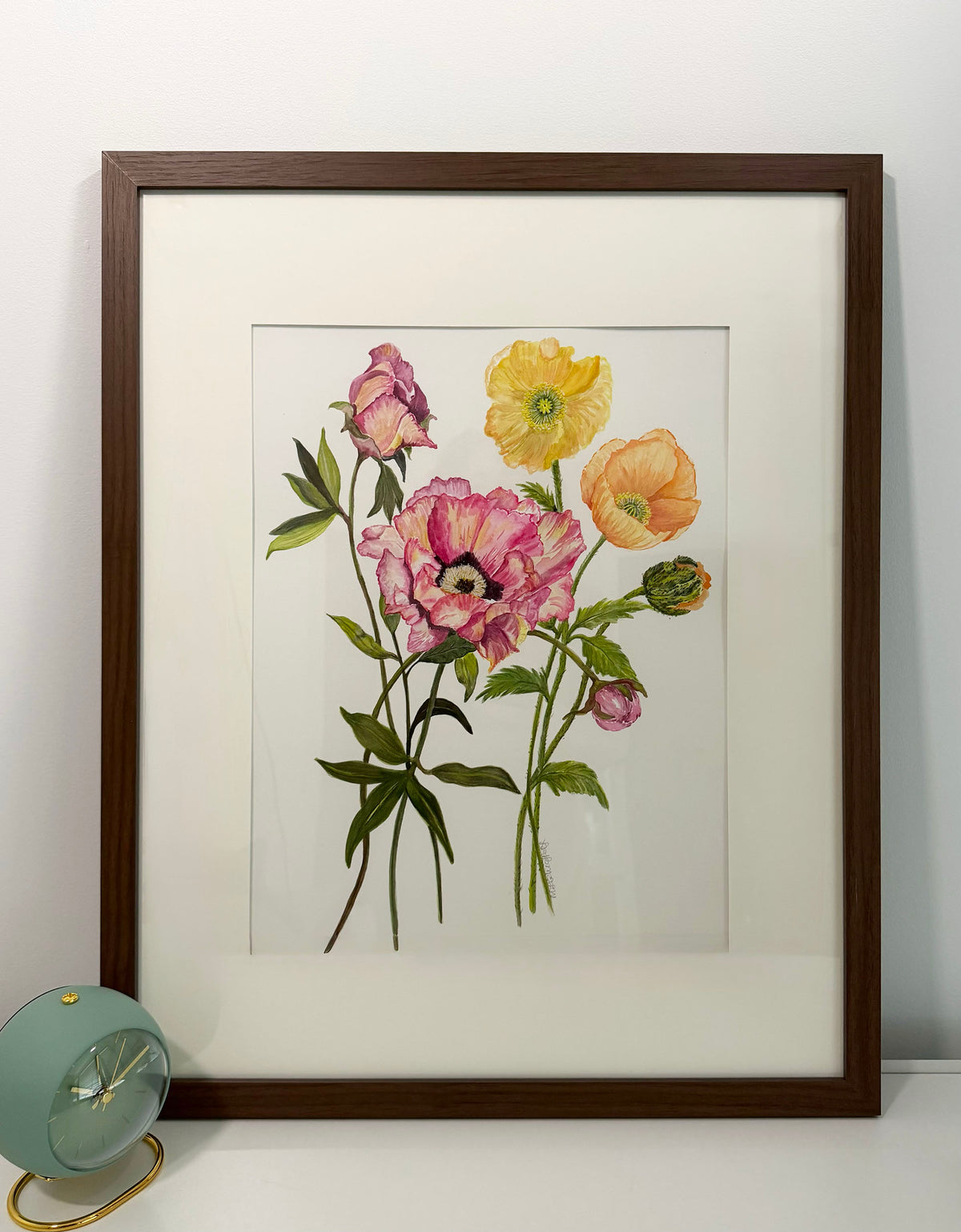 A framed botanical art print featuring pink, yellow, and peach flowers with green leaves, presented in a walnut wood grain frame with an off white mat  ready to hang.