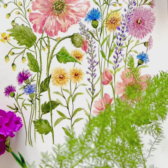 A video showing an expressive watercolour illustration of a wildflower bouquet. The composition includes a large, ruffled orange poppy and a soft peach flower, surrounded by smaller purple thistles, blue coneflowers, and delicate yellow blossoms with varied green foliage on a light off white back ground.